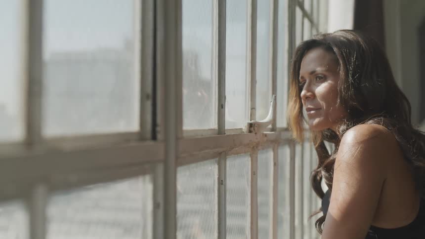 A young woman stands and looks out a window