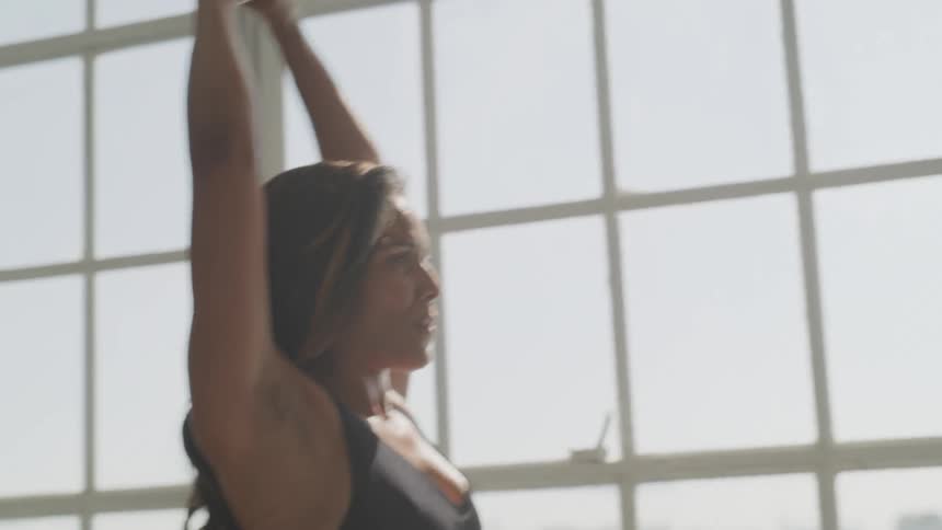 Brunette woman lifts kettlebell in front of the window on a sunny day