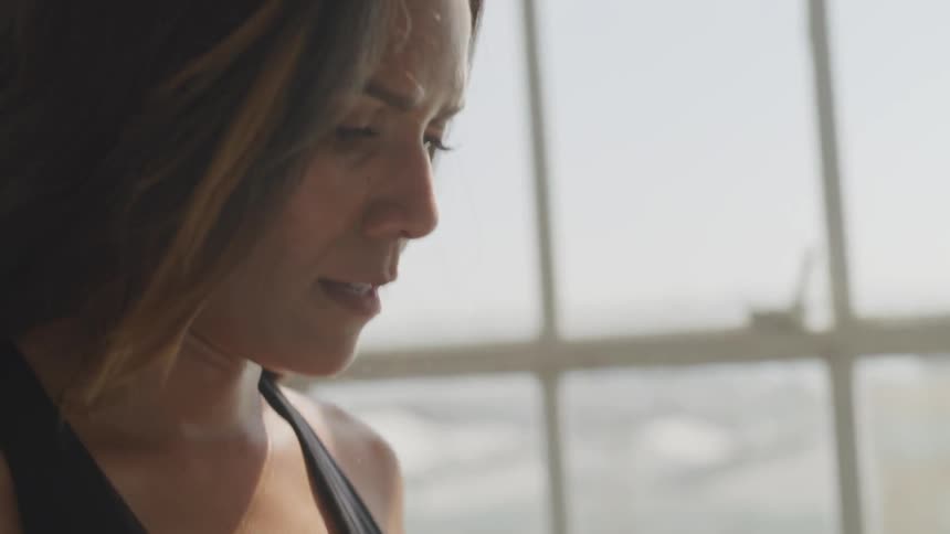 Sweaty brunette woman has a break during workout in front of arched window on a sunny day