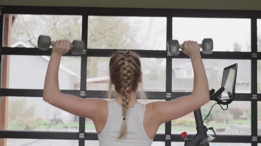 A woman lifts weights while staring out windows