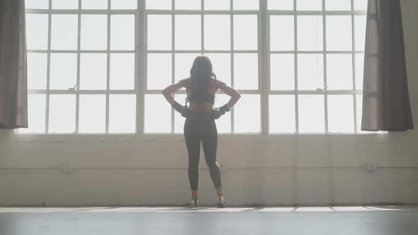 Woman wearing boxing gloves steps side to side and leans on wall