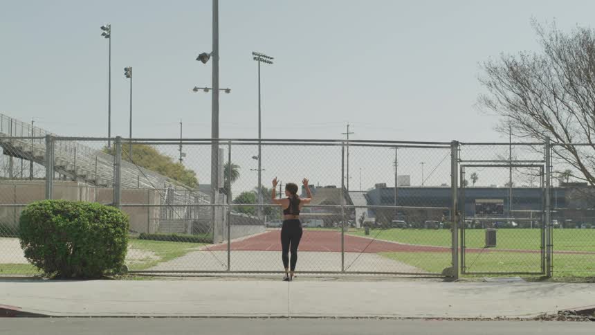 A young woman stretches against a wire fence