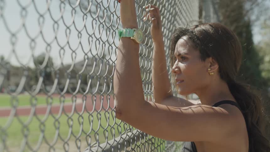 A woman looking through a chain link fence while holding onto it