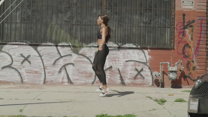 A woman jumps rope on a city sidewalk
