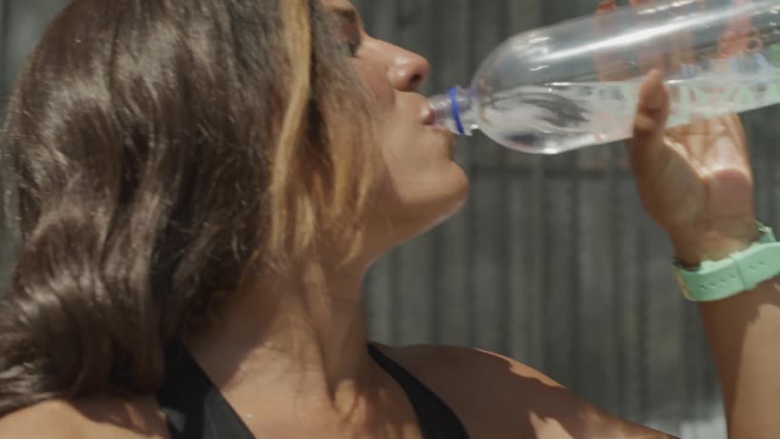 A woman in athletic clothing drinks water from a bottle