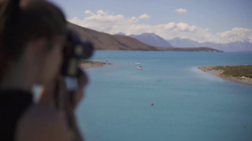 A woman is taking photographs of a lake on a sunny day