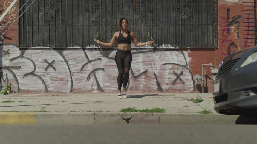 A young black woman jumps rope on a sidewalk