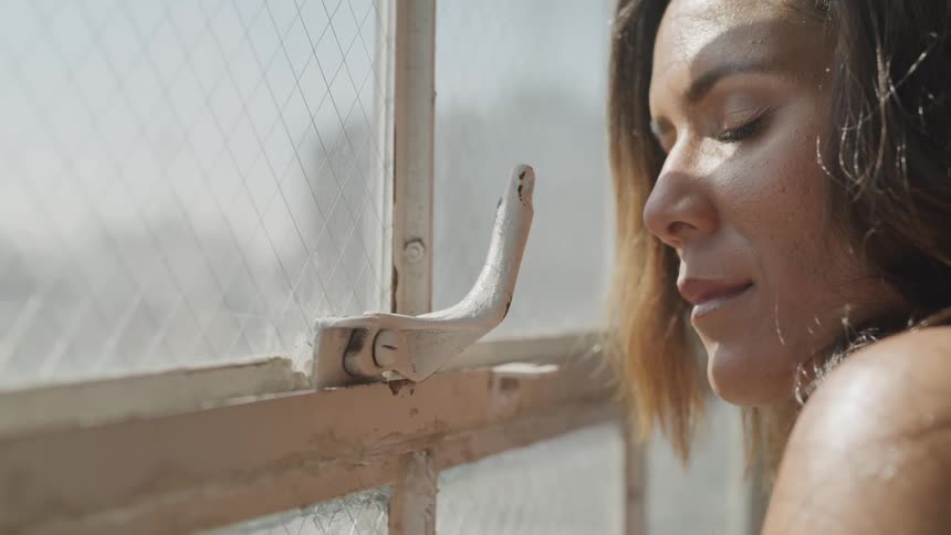 A woman is by a window with her eyes closed
