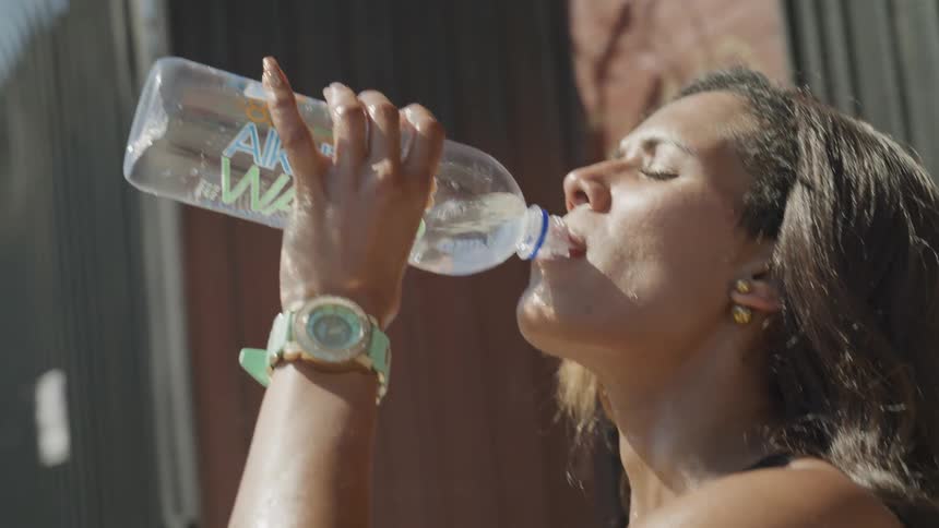 A black woman standing outdoors drinking a bottle of water