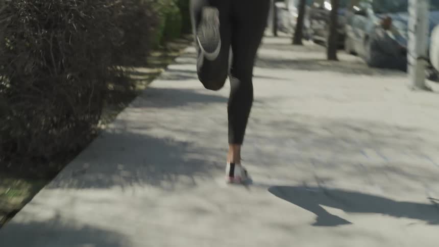 Brunette woman wearing tights runs along the pavement during daylight