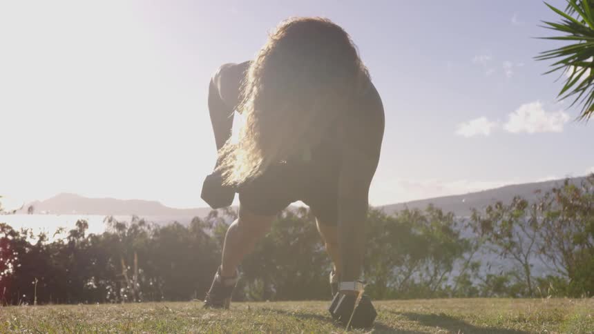Woman exercises with barbells outside with mountain in background
