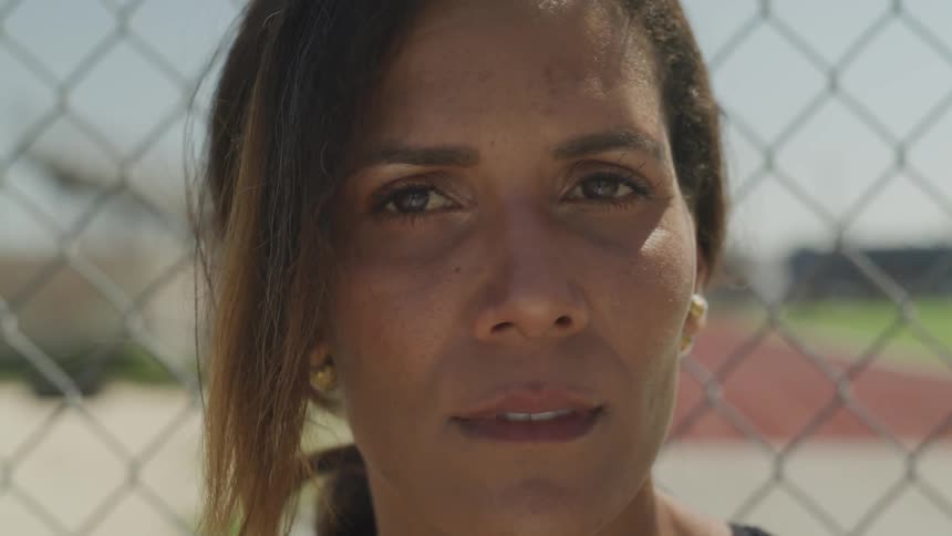 A woman looks into the camera while standing in front of a fence