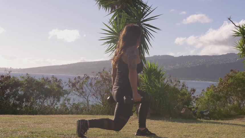 A woman is outdoors working out with weights
