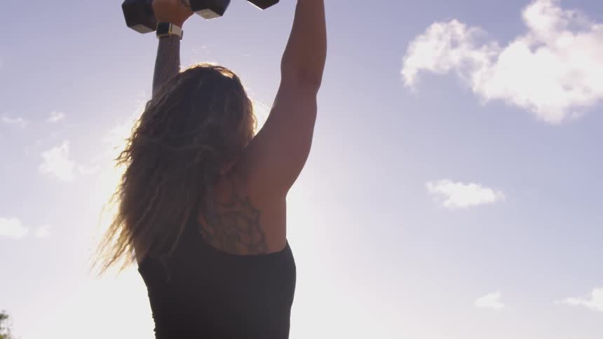 A woman does shoulder presses with weights outdoors