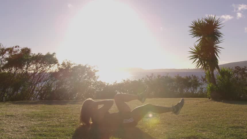 A young woman lies on the grass and does abdominal work