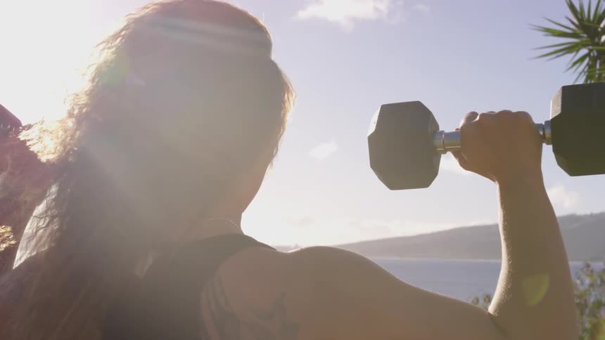 A young woman does shoulder presses outside