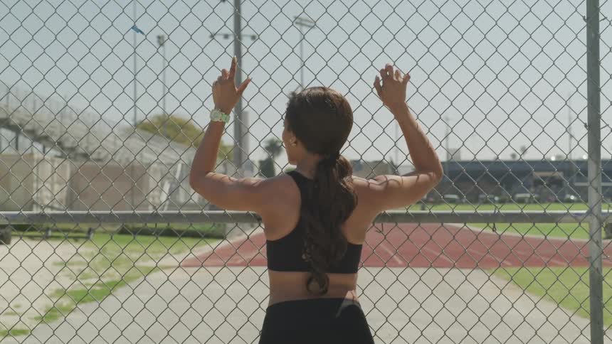 A woman leans against a fence looking out to a running track