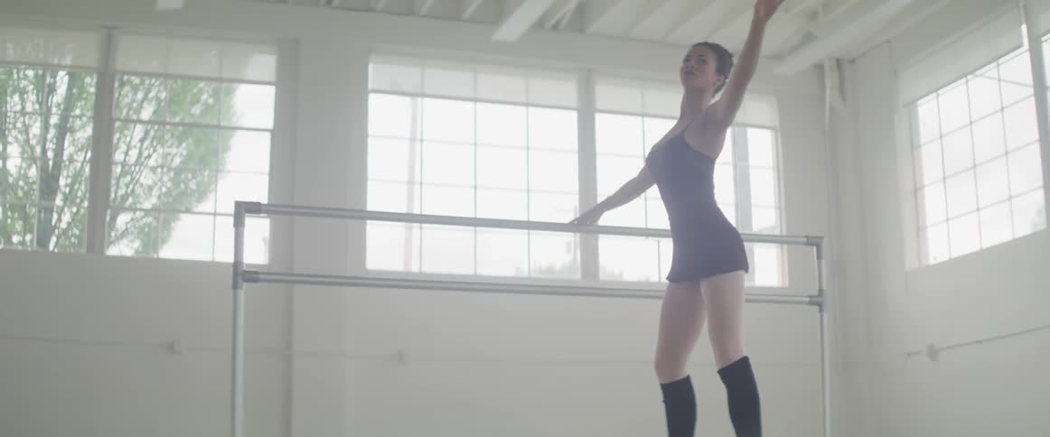 A woman in an indoor dance studio stretching next to ballet barres