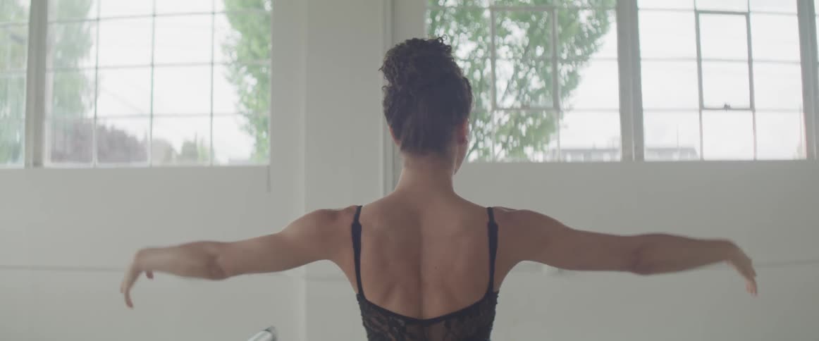 Ballet dancer wearing black ballet costume dances in front of arched window during daylight