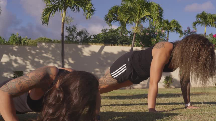 A pair of women doing push ups on a trimmed lawn