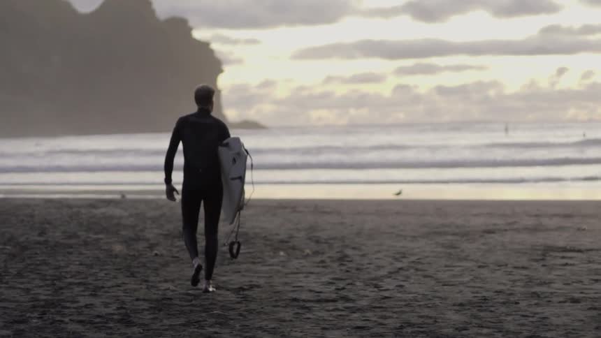 Man preparing his surfboard and wetsuit as he gets ready to surf by the ocean.