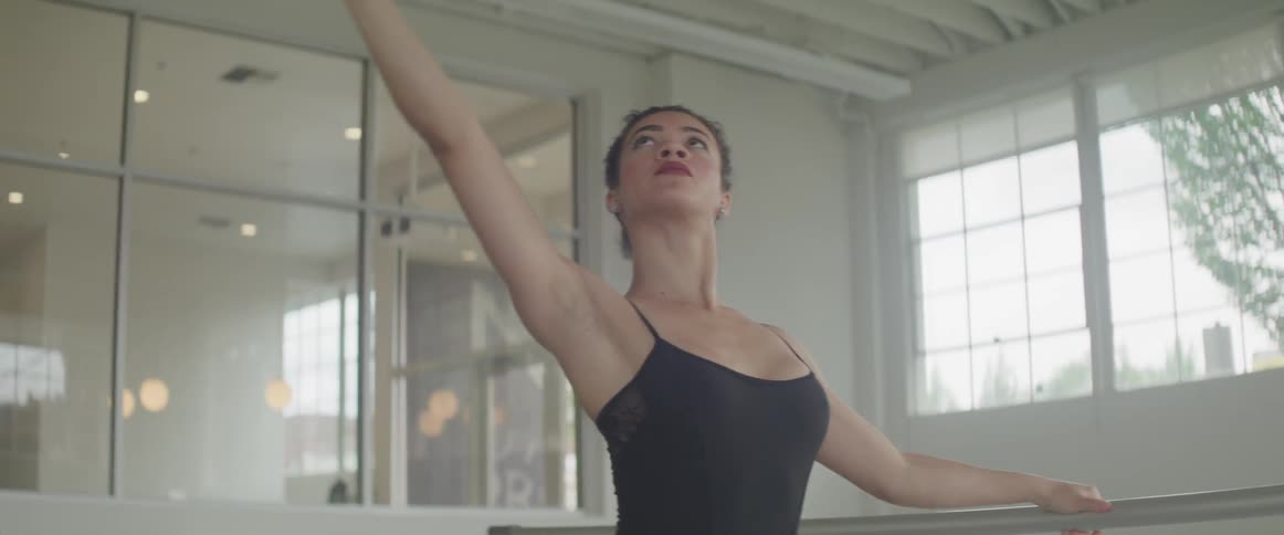 A young woman practices ballet in a dance studio during the day