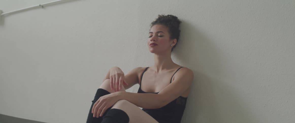A female ballet dancer leans against a wall under the bar in the studio and rests