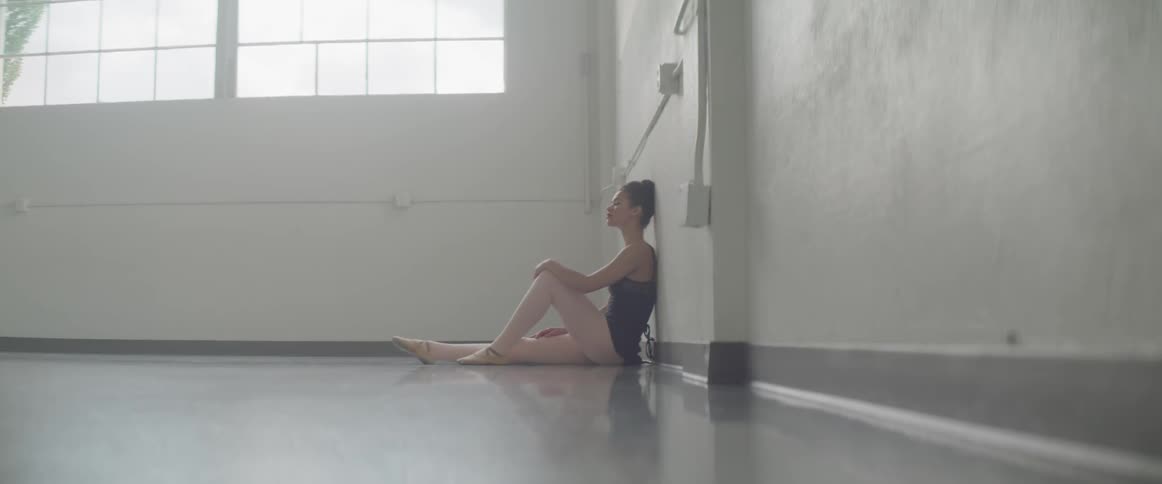 Female dancer relaxing on the floor against a wall after a workout