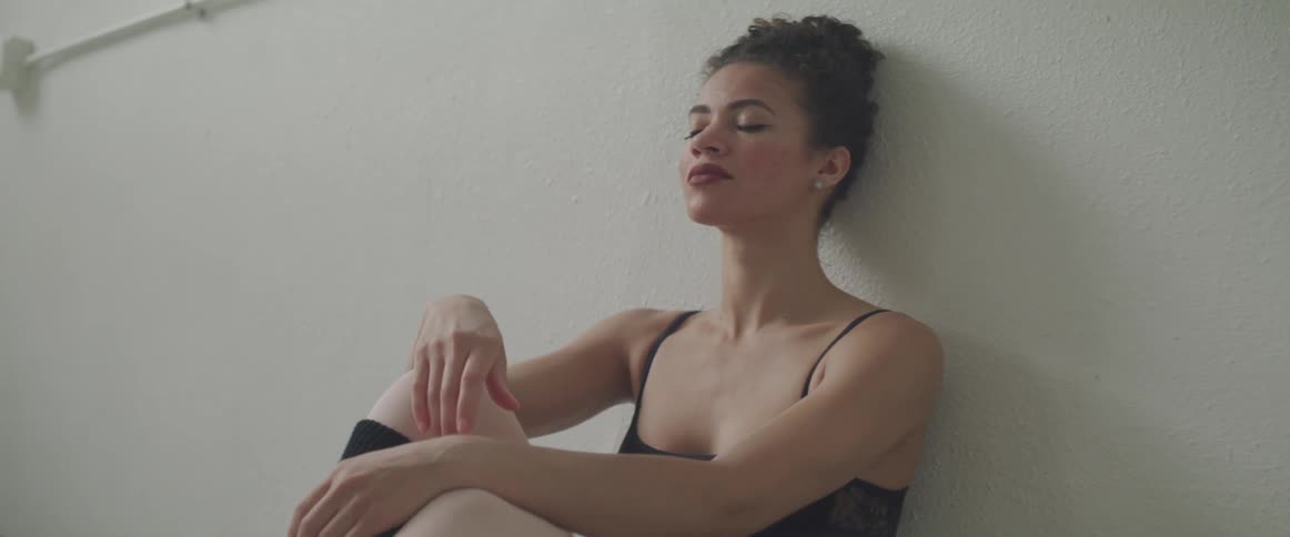Woman sits on floor and leans against white wall