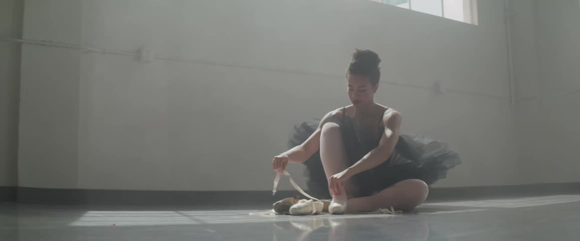 Ballerina dancer sitting on floor putting on ballet shoes