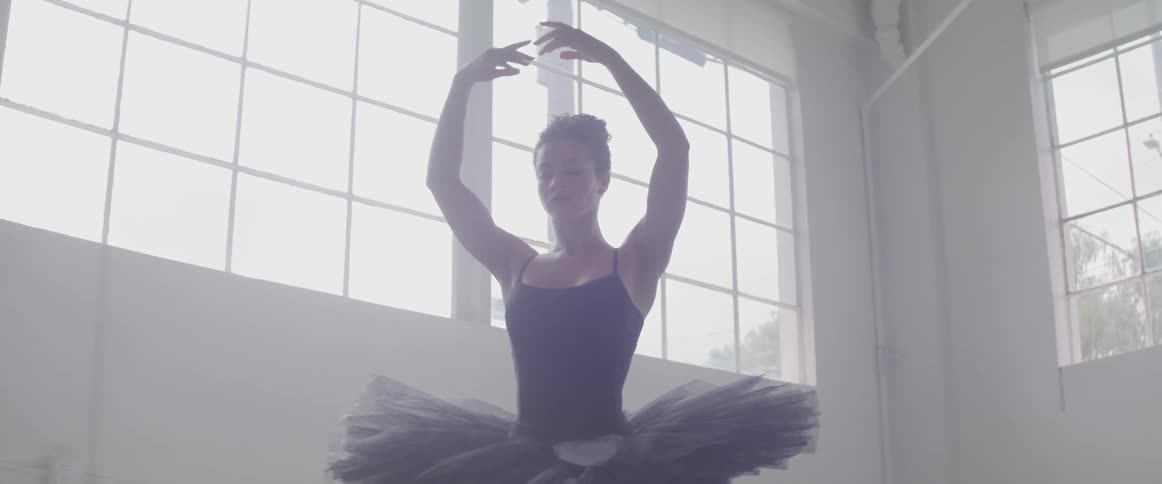 Ballet dancer wearing black ballet costume dances indoors during daylight