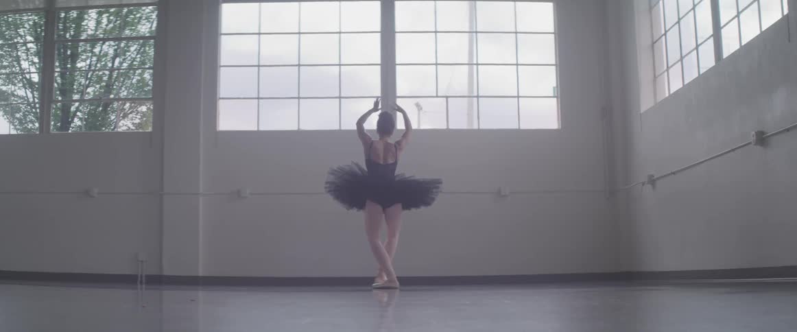 A ballerina in a black tutu posing in a studio with large windows