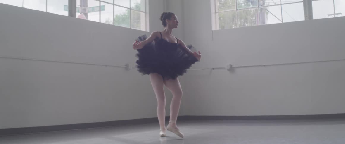 Ballerina in a black tutu practicing jumps in a studio