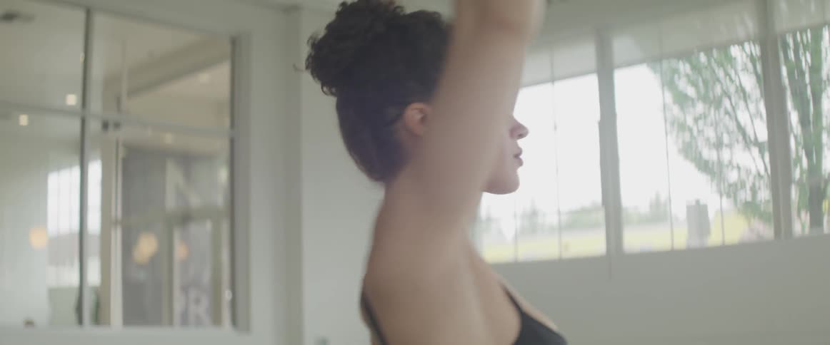 A dancer raises her arms overhead spins to face the opposite direction and gracefully lowers her arms in front of a mirror in a dance studio