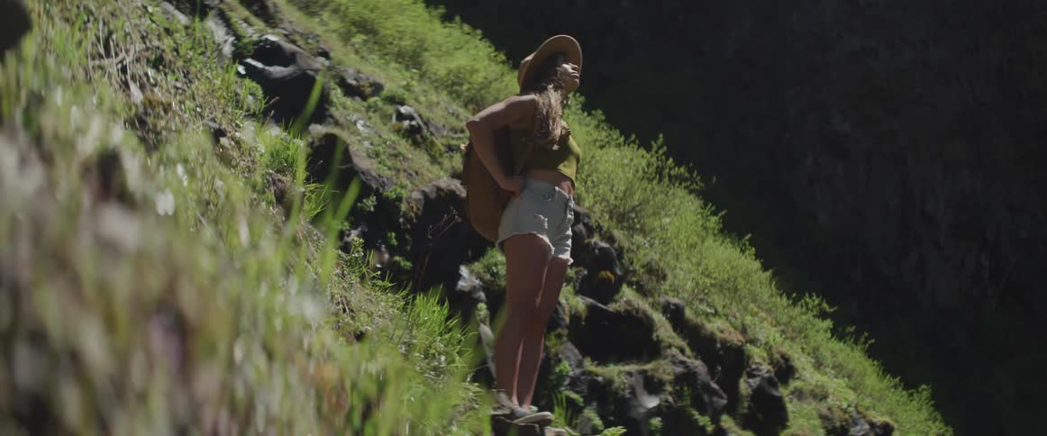 A woman in denim shorts stands on a hillside and looks up to the sky