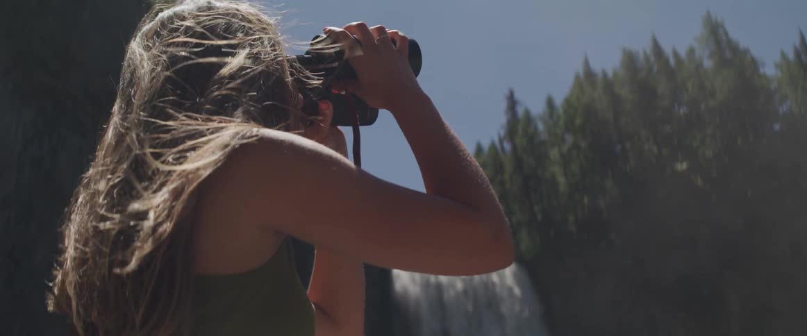 A woman holds binoculars to her face to look at the sky