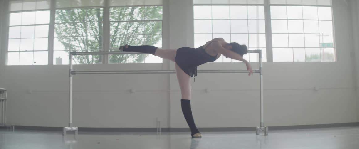 A ballerina stretches with one leg on the bar as she reaches for the floor and then back up