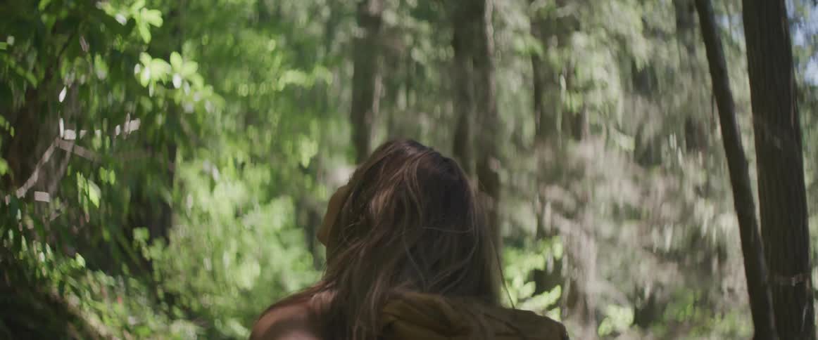 A backpack wearing woman turns around in a forest scene