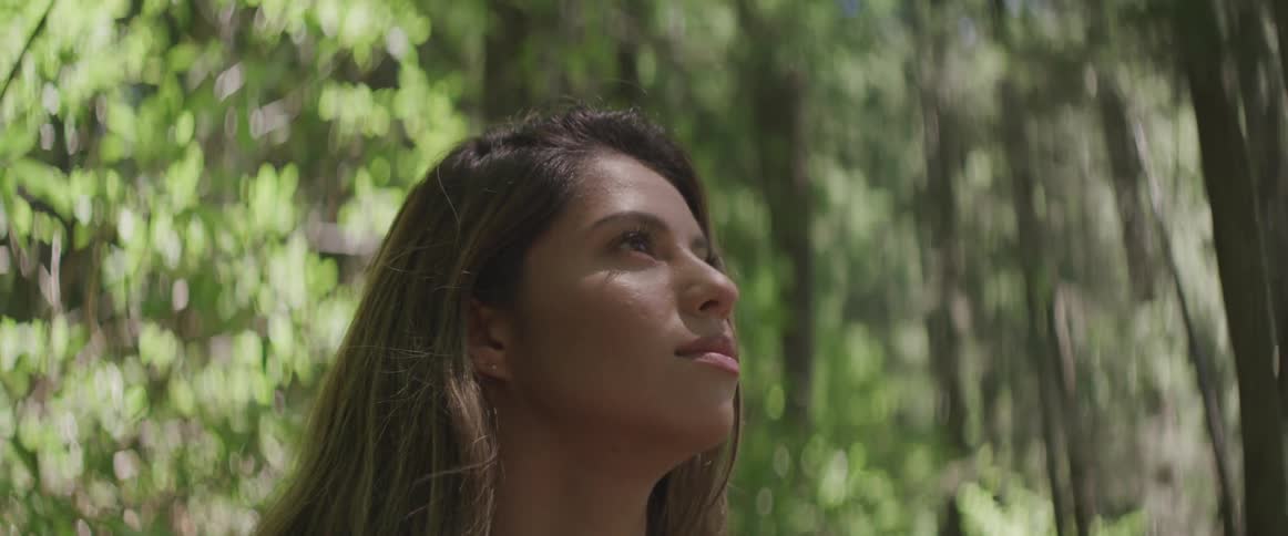 A young woman stands in a forest and looks off in to the distance