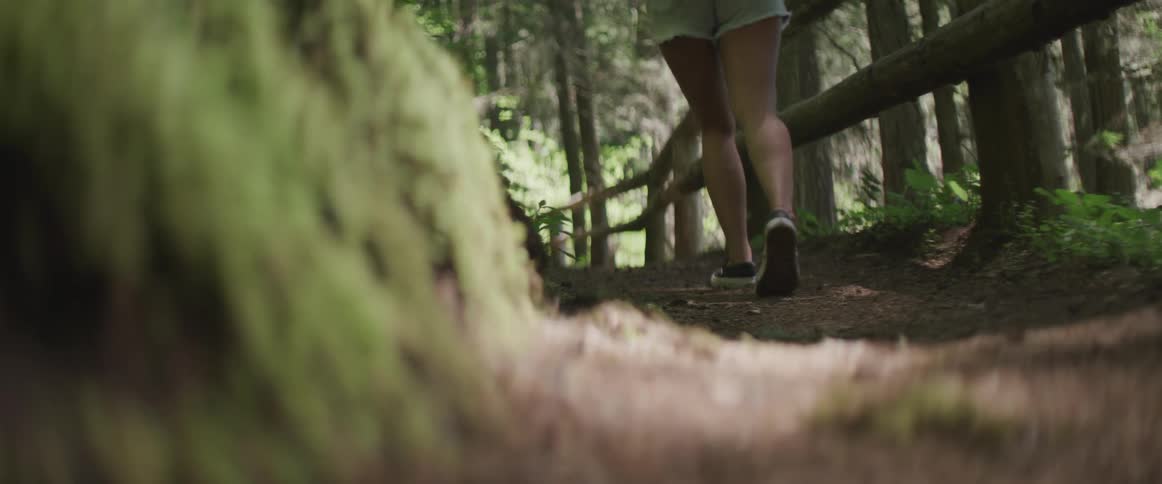 Woman wearing mini shorts walks on the forest path in the dense forest during daylight