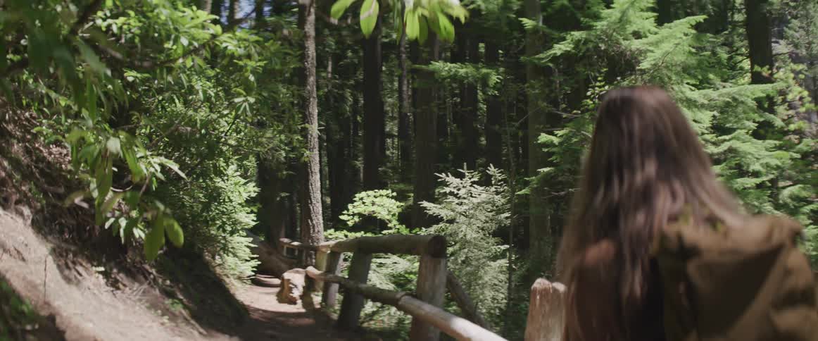 A woman in a vest with a backpack walks through a forest path