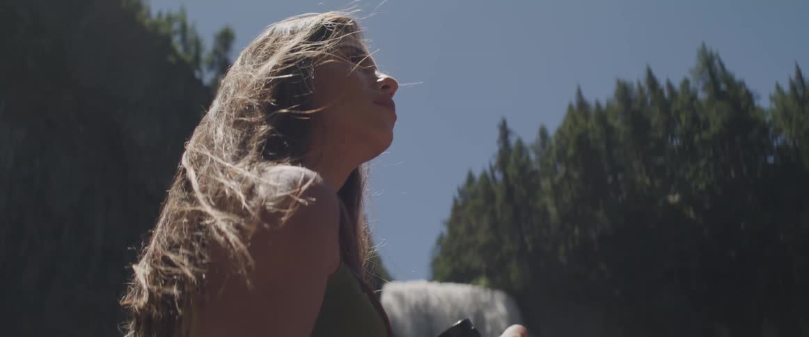 Woman sits in a forest with a waterfall nearby