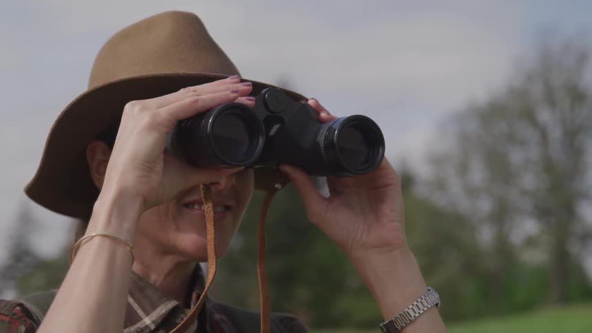 A woman looks through binoculars as she stands outside