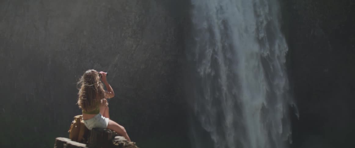 A female is sitting on a ledge and looking at a waterfall