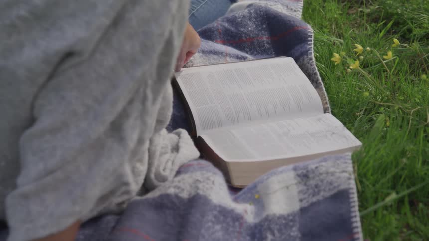 A person reading a book while sitting on a blanket in a field