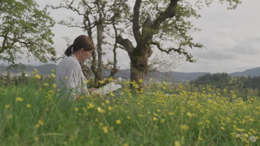 A woman sits and reads a book in an open field