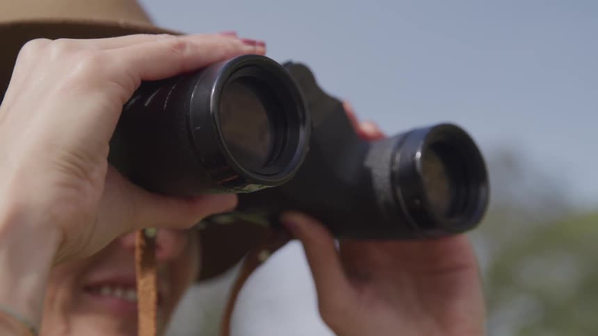 Woman looking through binoculars outdoors slowly lowers them