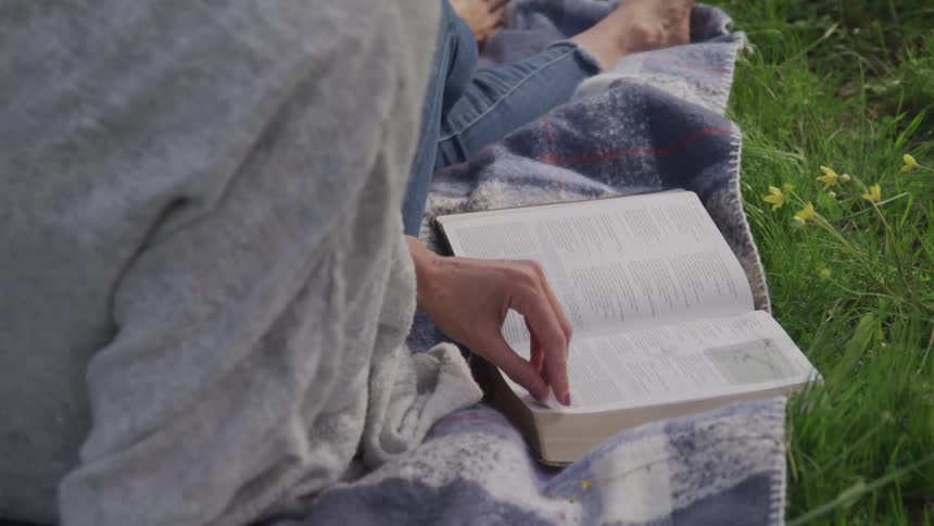Woman sits on the green grass and reads book during daylight