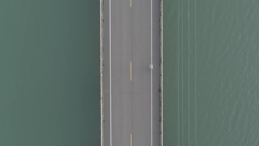 A motorcycle rides across a long narrow bridge
