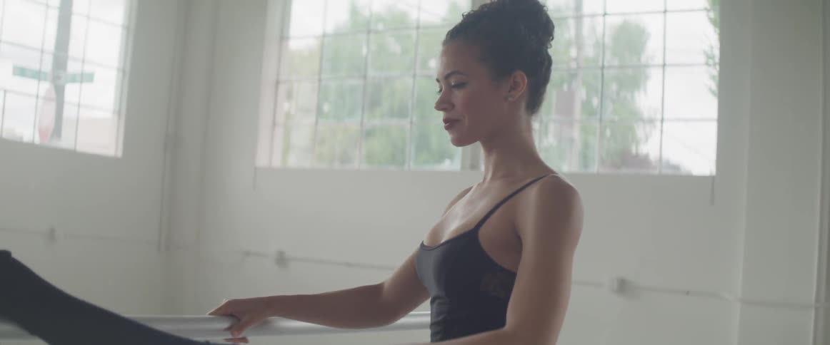 A ballet dancer lifts her leg onto a barre and stretches